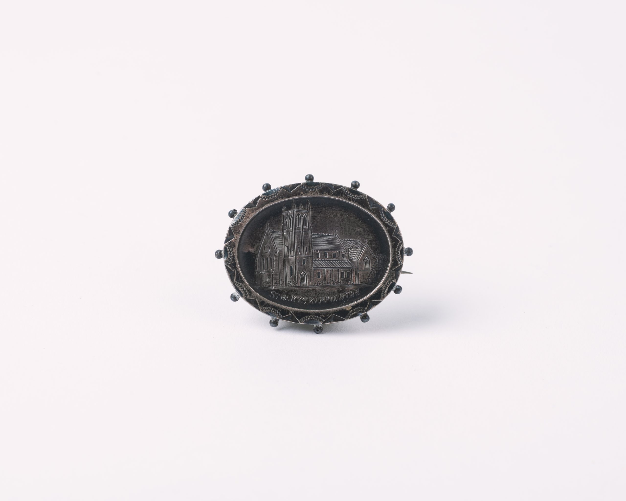 Image of small silver brooch, engraved on the surface is the image of a church