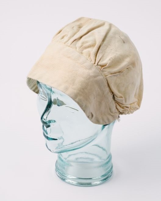 Image shows a bonnet style cap. The cap is cream with discolouration.