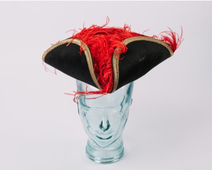 Image shows and elaborate black tricorn hat with gold braiding and red plumage. 