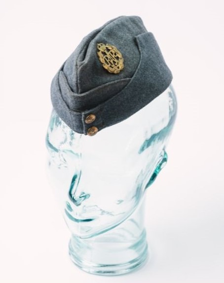 Image shows a navy side cap with a brass king's crown badge to the side.